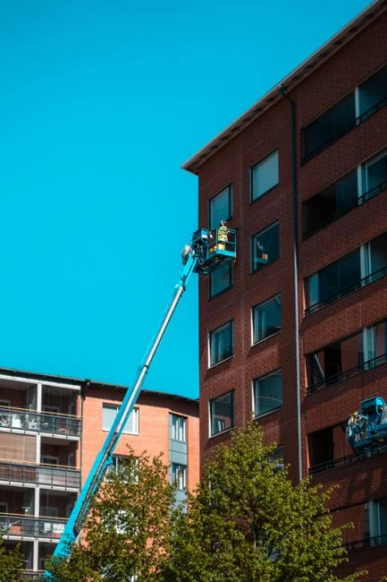 gallery-03 A man cleaning skyscraper windows with a harness, showcasing urban high-rise work.